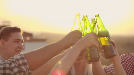Junge-Leute-Stoßen-Auf-Einer-Party-Mit-Freunden-Auf-Dem-Dach-An-Und-Trinken-Kaltes-Bier-Aus-Bunten-Grünen-Flaschen.